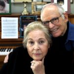 Alan and Marilyn Bergman sit closely in front of their piano at home