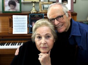 Alan and Marilyn Bergman sit closely in front of their piano at home