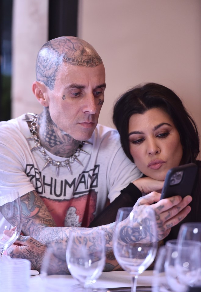 Travis Barker and Kourtney Kardashian looking at a cell phone.