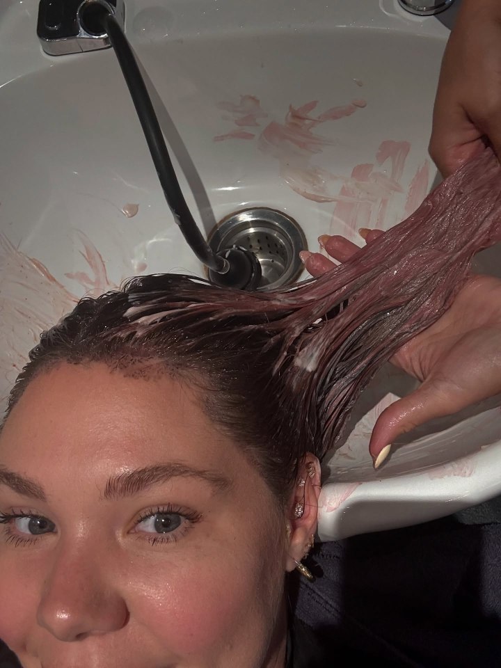 Woman rinsing pink hair dye from her hair in a sink.