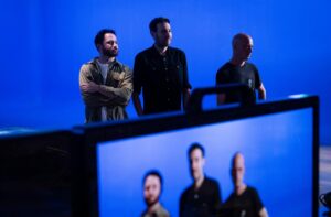 Three men standing against a blue screen background in a studio