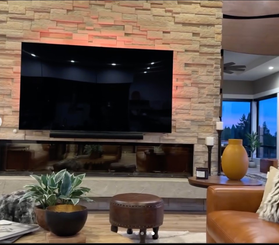 Living room with large TV above fireplace and stone wall.