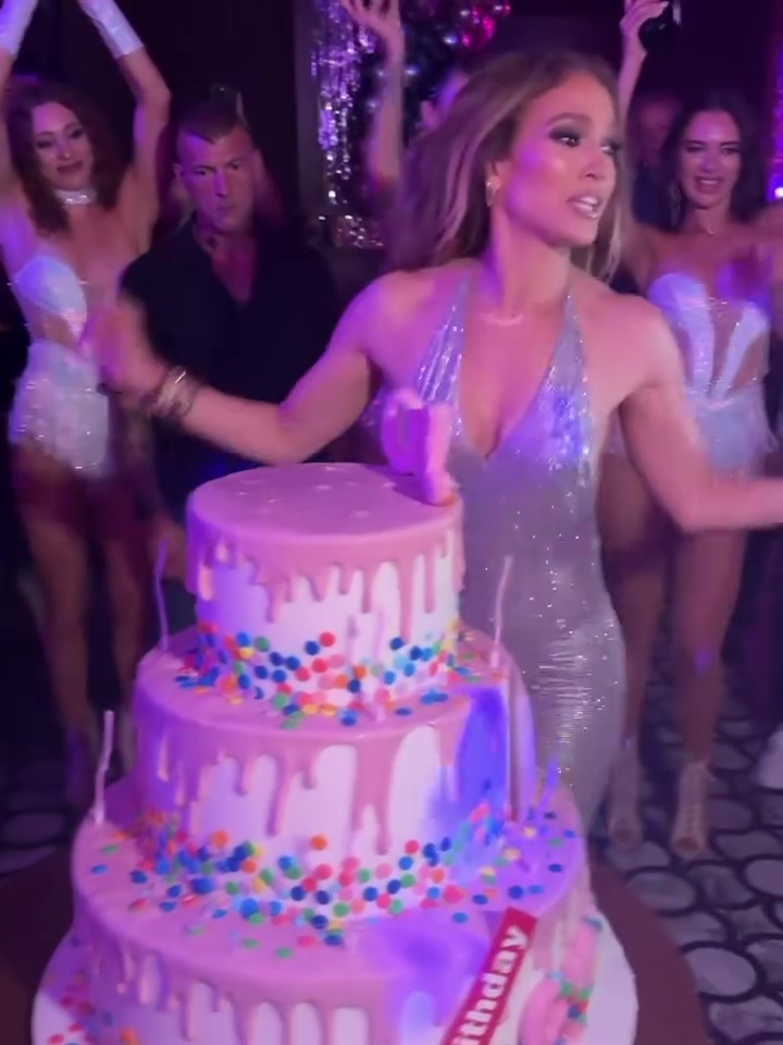 Jennifer Lopez at her birthday celebration with a large multi-tiered cake.