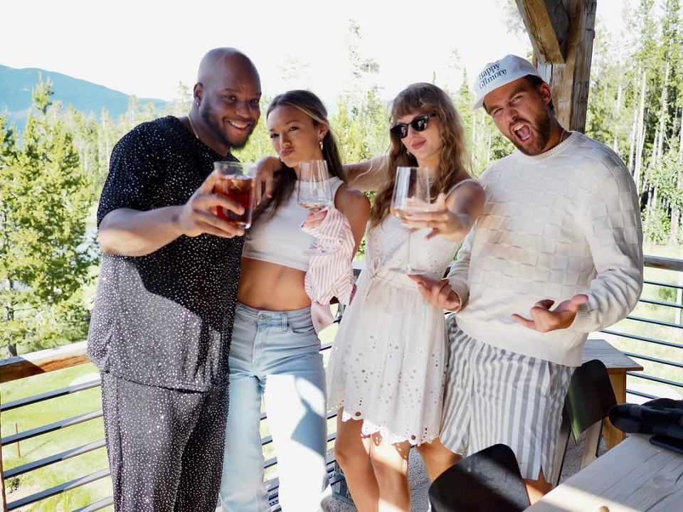 Four friends posing on a balcony with drinks.