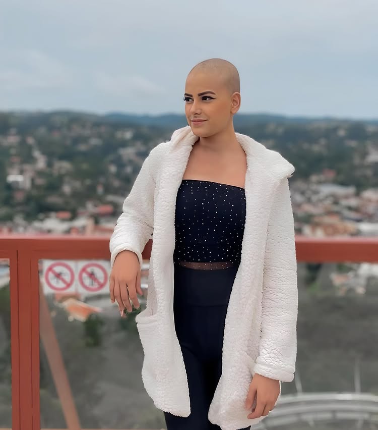 Woman with shaved head wearing a white coat and black top.