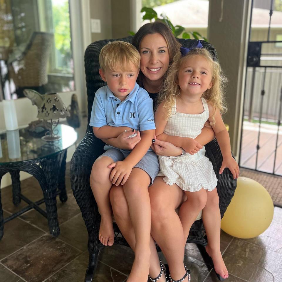 Woman sitting in a chair with two young children on her lap.