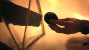 A human hand holds out a little ball to a rock-like hand behind a screen