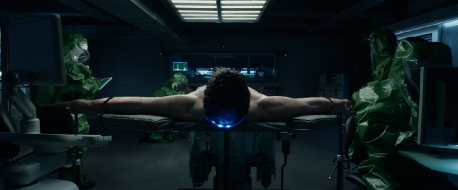 Reed Richards, played by Miles Teller, is strapped to a table with his arms stretched in a scene from the 2015 Fantastic Four movie. 