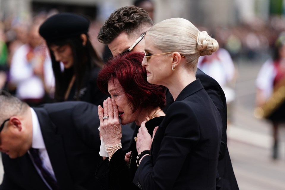 Sharon and Kelly Osbourne view floral tributes at a memorial.