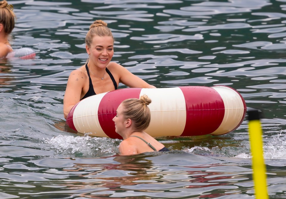Duas mulheres em roupas de banho desfrutando de uma piscina flutuando em um lago.