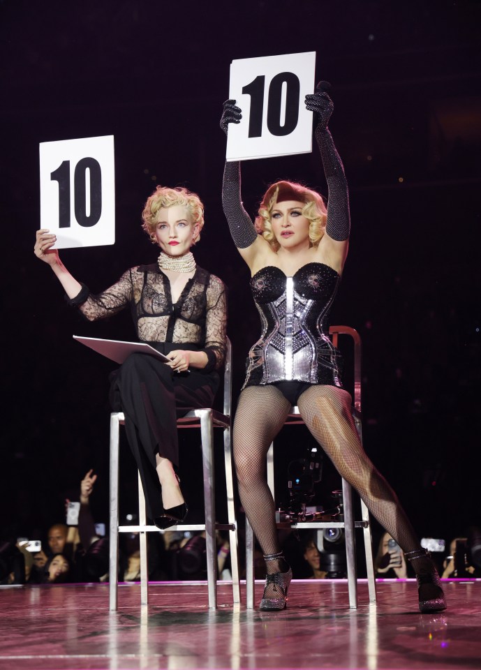 Madonna e Julia Garner em um concerto, segurando scorecards que leem "10".
