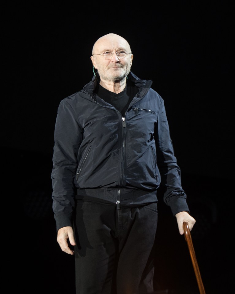 Phil Collins performing on stage with a cane.