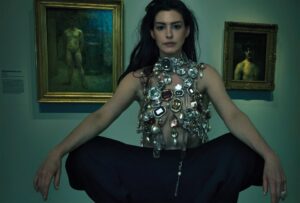 Woman wearing a large jeweled necklace in front of paintings.