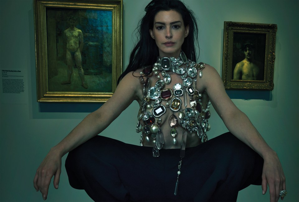 Woman wearing a large jeweled necklace in front of paintings.
