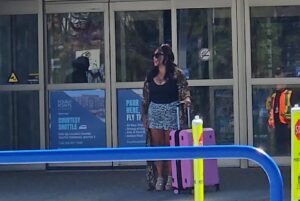 Woman with luggage at airport entrance.