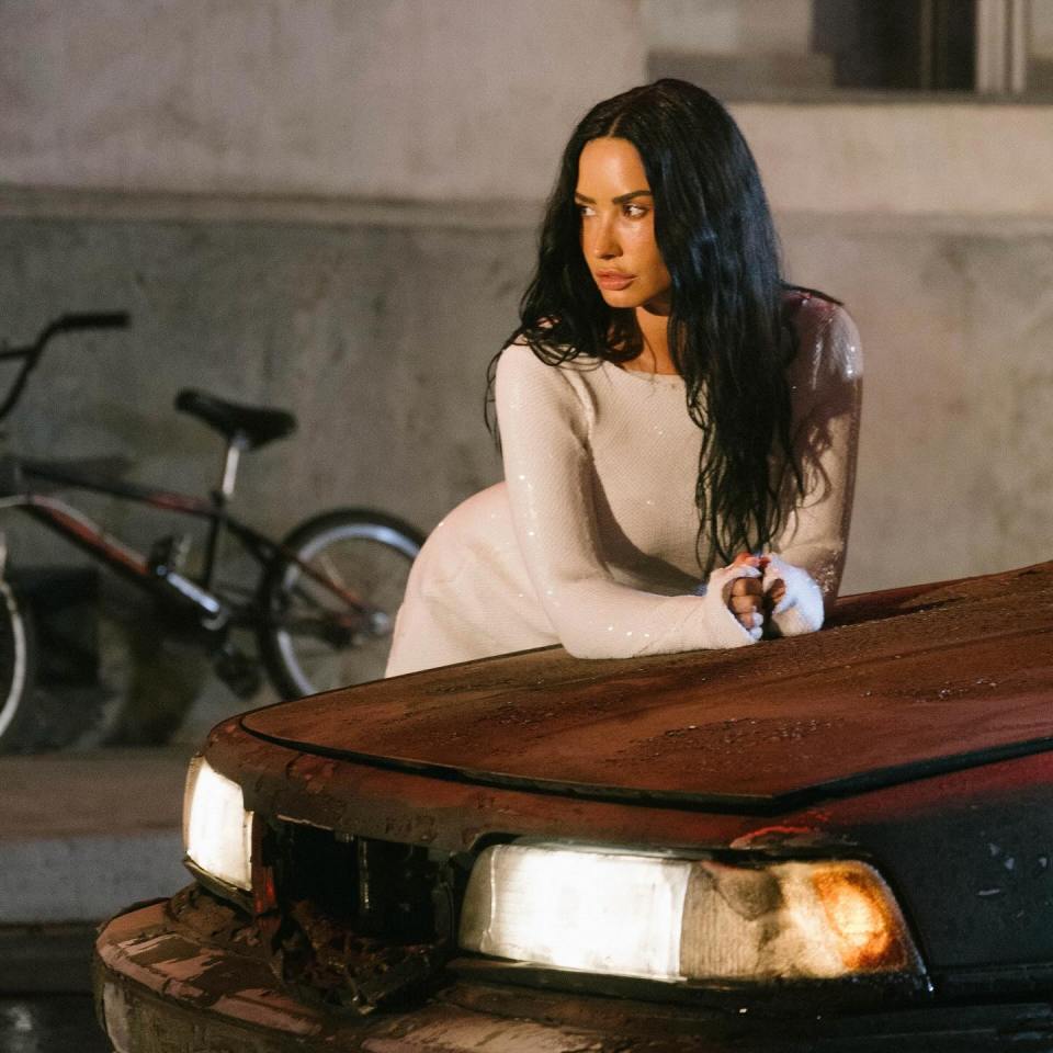 Demi Lovato leaning on a damaged car.