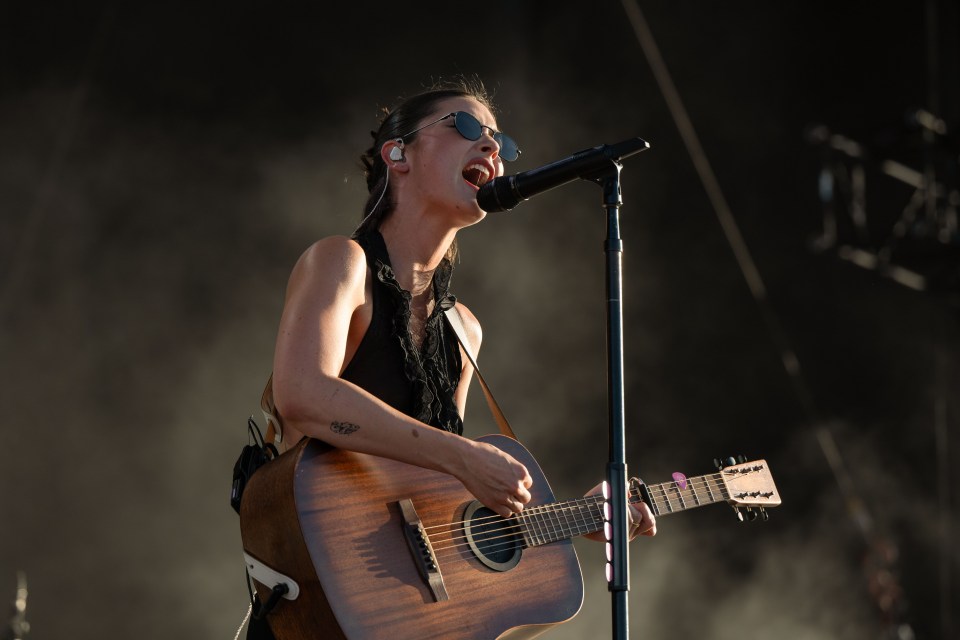 Gracie Abrams performing at a music festival, playing acoustic guitar and singing into a microphone.