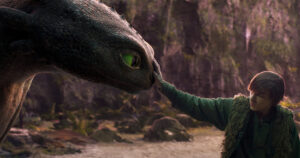 Hiccup (Mason Thames) hesitantly reaches out to touch the snout of Toothless the black dragon in the live-action How to Train Your Dragon