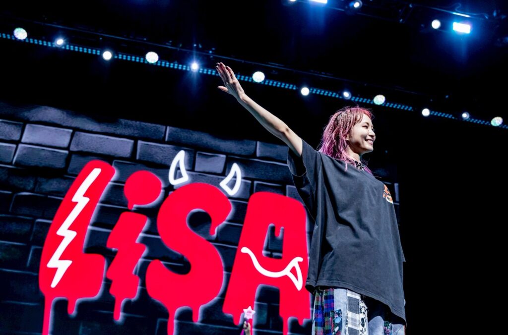 J-pop musician LiSA, on stage with a huge red sign featuring her name — with little devil horns on the “S” — in the background