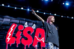 J-pop musician LiSA, on stage with a huge red sign featuring her name — with little devil horns on the “S” — in the background