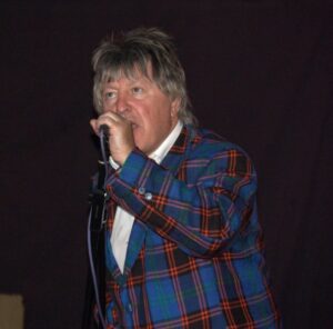 Jock McDonald, a legendary Scottish musician, singing into a microphone.