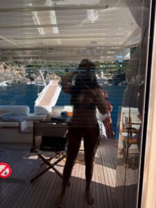Reflection of a woman in a bikini taking a selfie on a yacht.