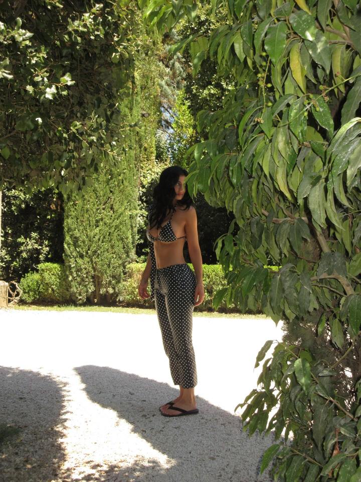 Woman in polka dot bikini and pants standing outdoors.