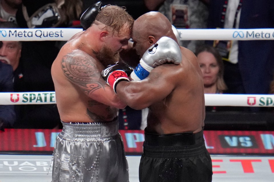 Jake Paul and Mike Tyson embracing in a boxing ring.