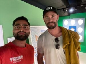 Chris Hemsworth and a man in a red shirt pose for a selfie.