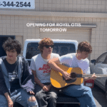 Three young men sitting on the back of a truck, playing a guitar; announcement for upcoming performance opening for Royel Otis.