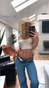 Olivia Dunne taking a selfie while wearing a tiny beige tube top and unbuttoned denim jeans.