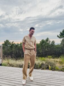 Ryan Seacrest in a tan suit, standing on a deck.