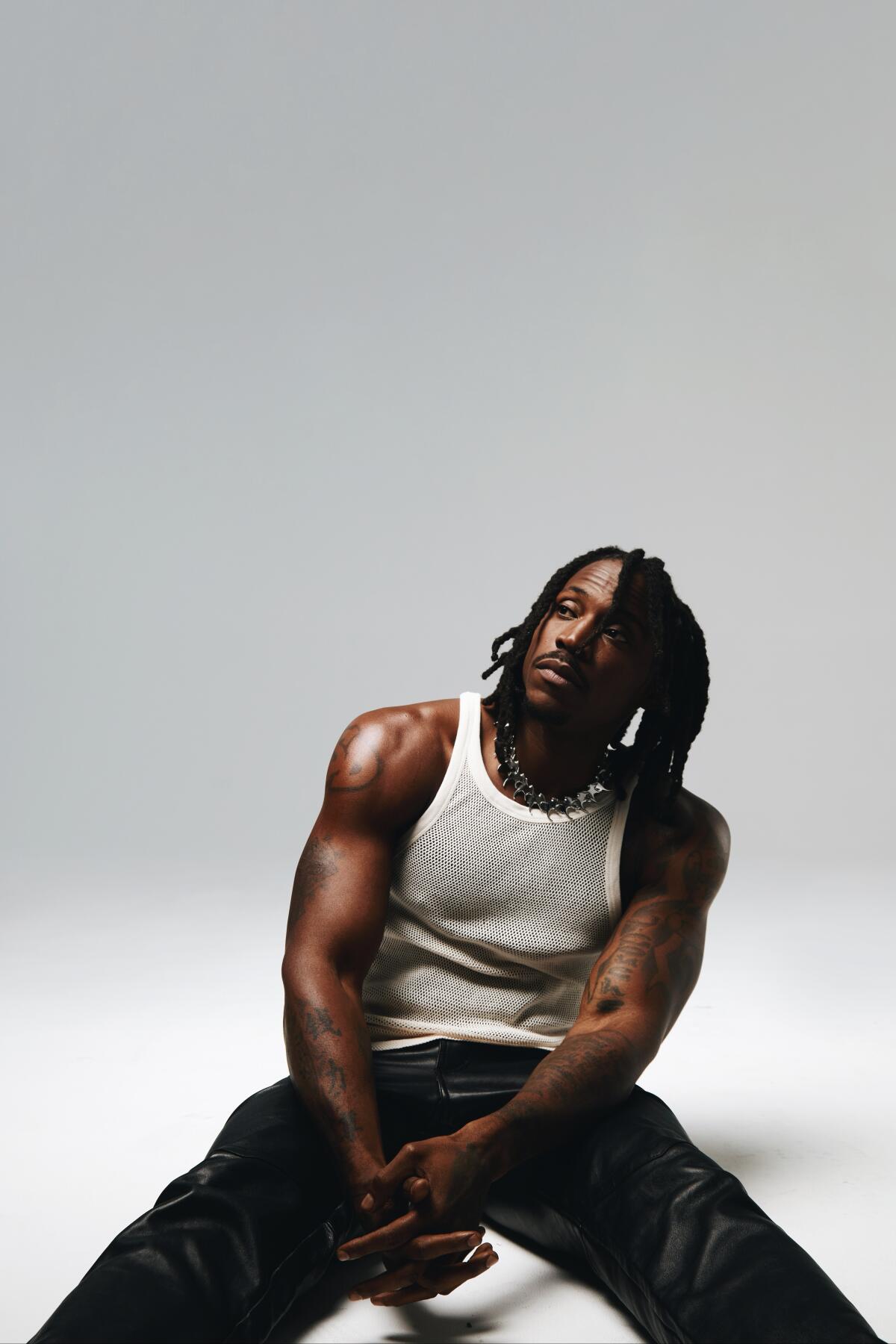 Man in a tank top sitting on the floor of a white room
