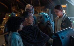 Jude Law Jedi huddles with some kids including a kid Ortolan aka Baby Max Rebo in a spaceship cockpit in Star Wars: Skeleton Crew