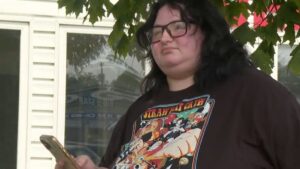 Woman in black t-shirt and black hair holding phone up under tree