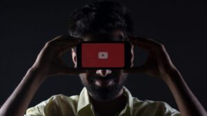 A photo of a man holding up the YouTube application on a smartphone.