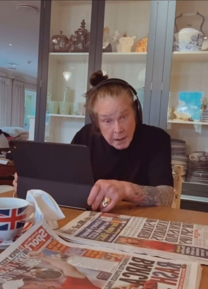 Ozzy Osbourne in a video, looking at a tablet and newspapers.