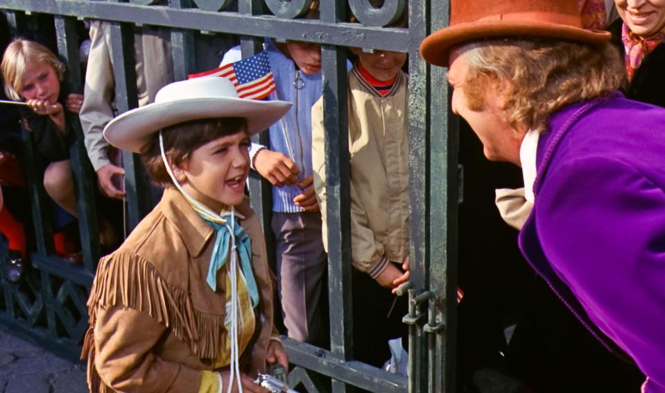 Scene from Willy Wonka & the Chocolate Factory: Willy Wonka speaks to a boy through a gate.