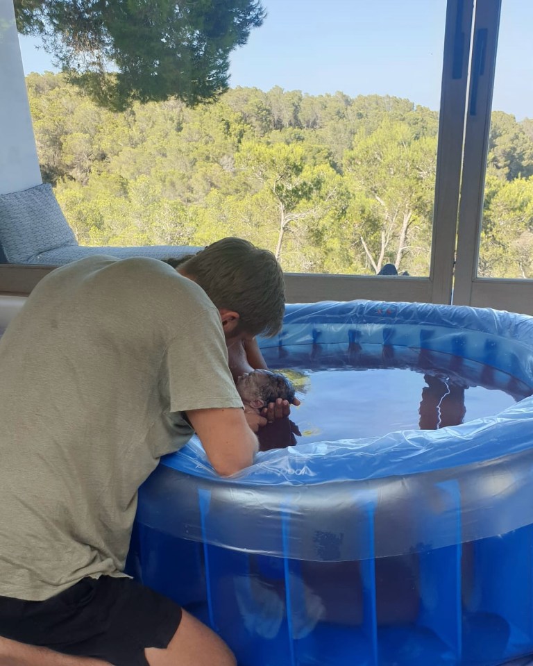 Person leaning over a birthing pool holding a newborn baby.