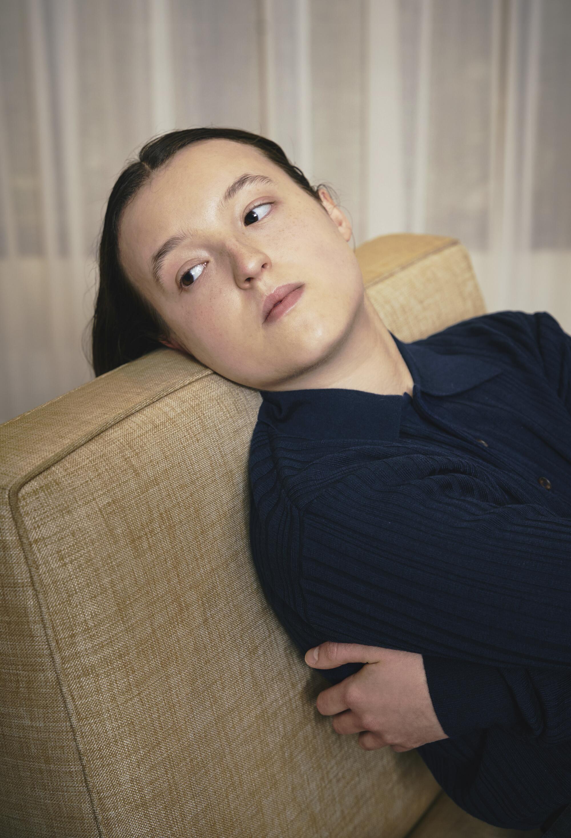Bella Ramsey leans back on a sofa.