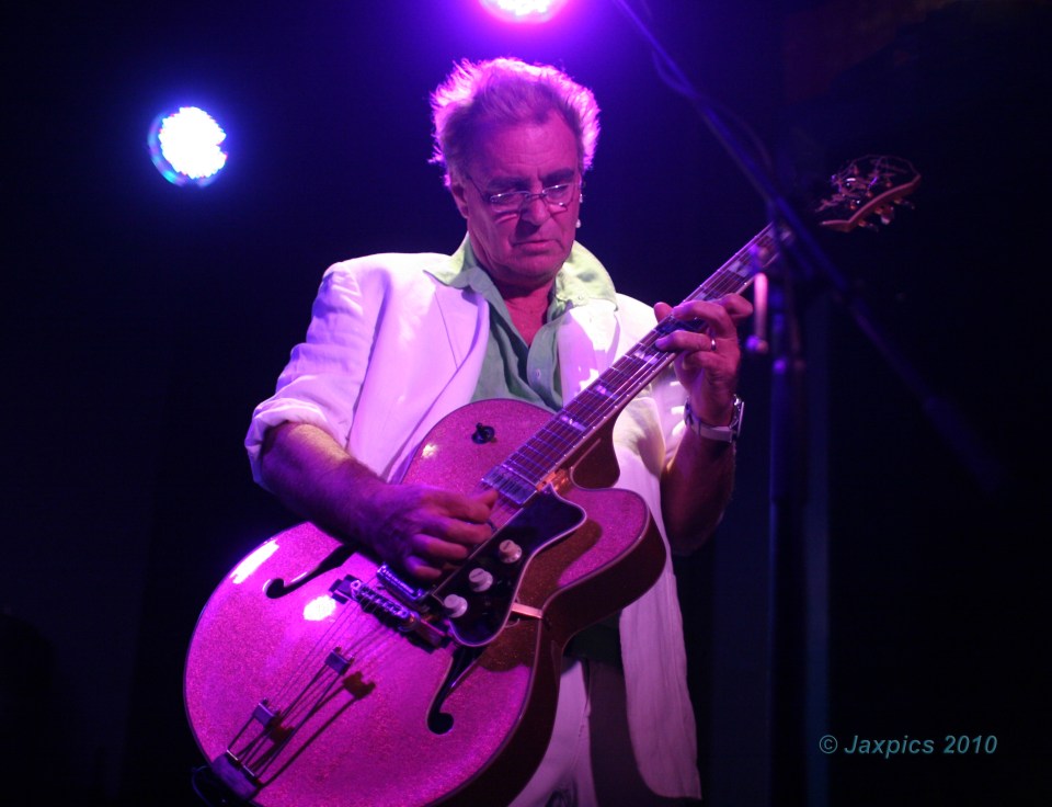Man playing pink guitar on stage.