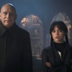 Uncle Fester and Wednesday Addams stand next to each other in a hallway