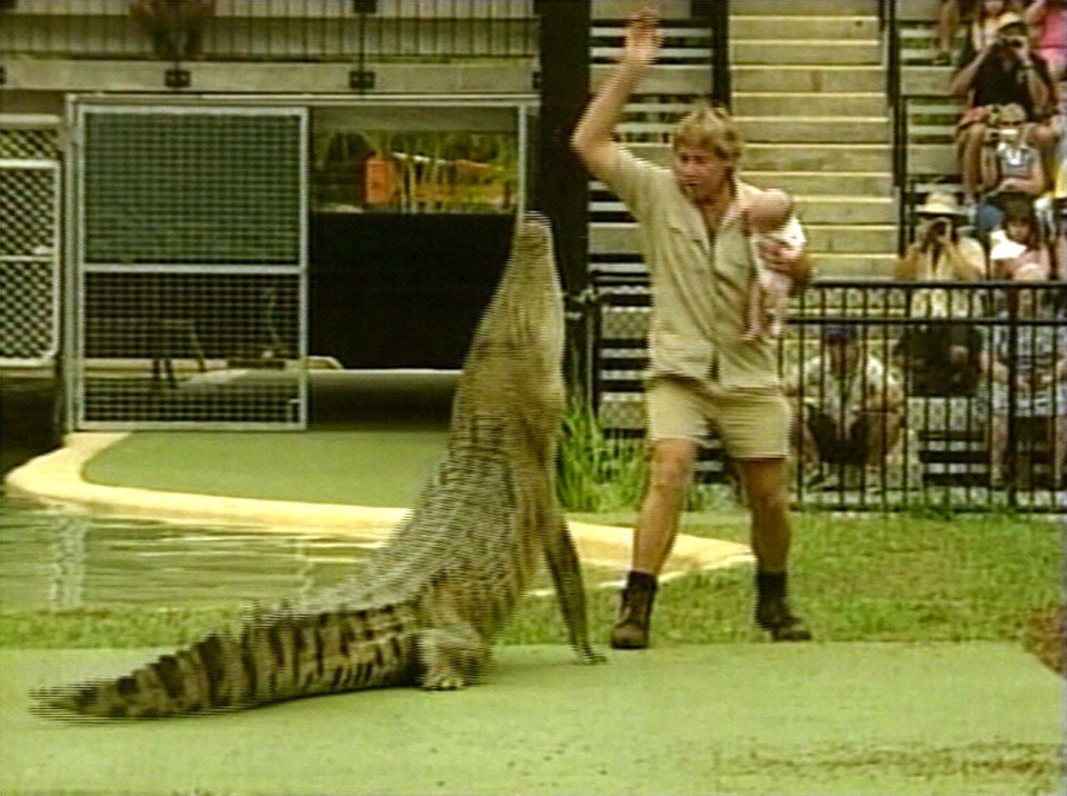 Steve Irwin holding his baby son while feeding a crocodile.