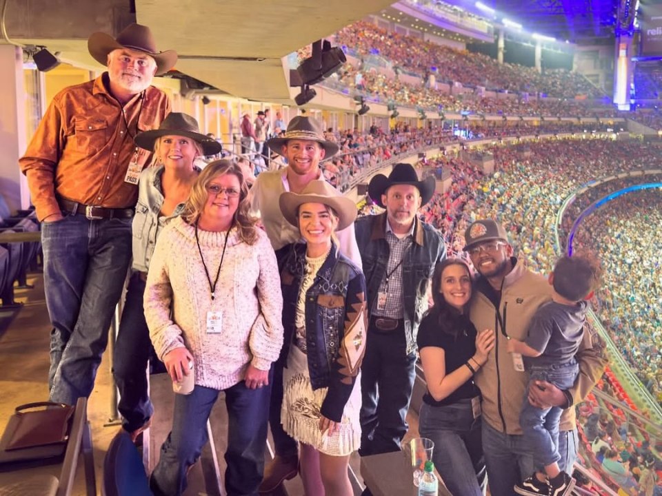 Group photo of people wearing cowboy hats at a rodeo.