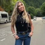 Woman with long blonde hair wearing a black top, jeans, and a Gucci belt.