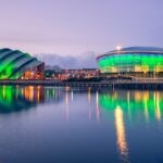 The Armadillo and Scottish Hydro Arena in Glasgow at night, illuminated green and reflected in the water.