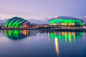 The Armadillo and Scottish Hydro Arena in Glasgow at night, illuminated green and reflected in the water.